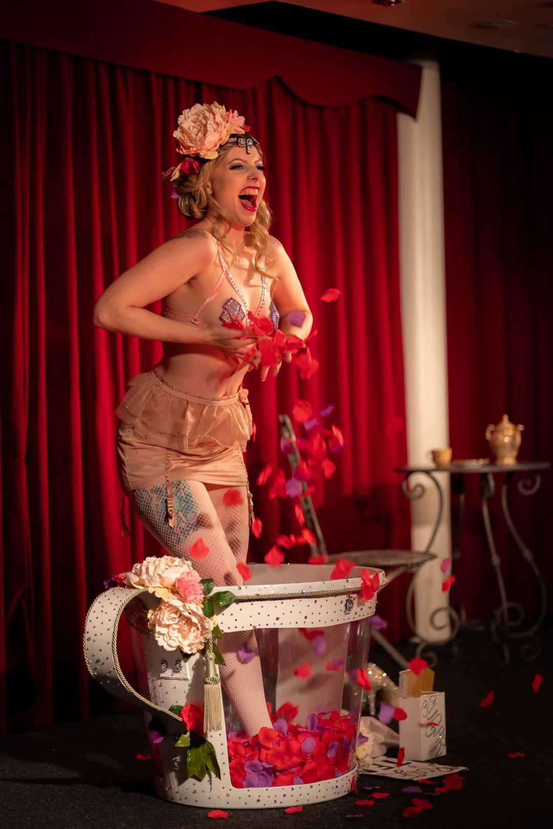 Burlesque performer on stage standing in a huge teacup with rose petals