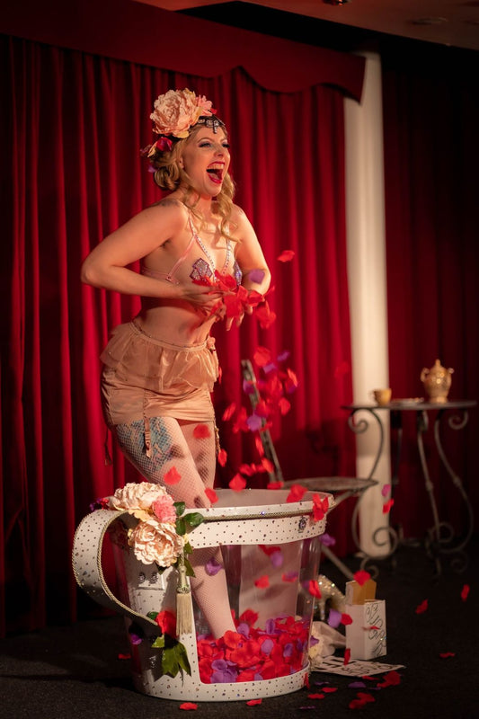Burlesque performer on stage standing in a huge teacup with rose petals